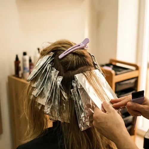 Papeles de aluminio colocados en secciones de cabello rubio, con una pinza lila sujetando