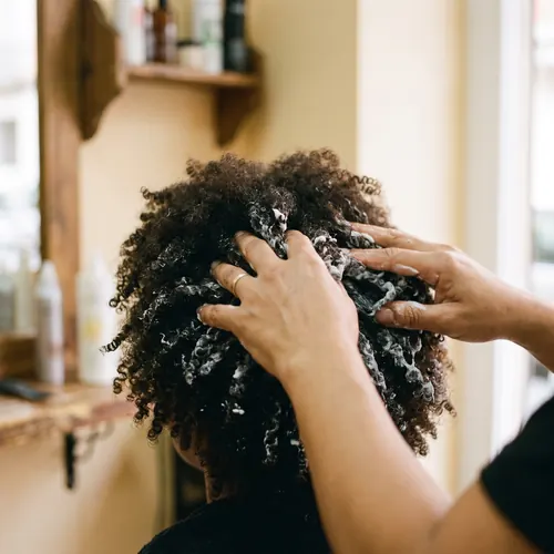 Manos aplicando mascarilla hidratante sobre cabello rizado y denso
